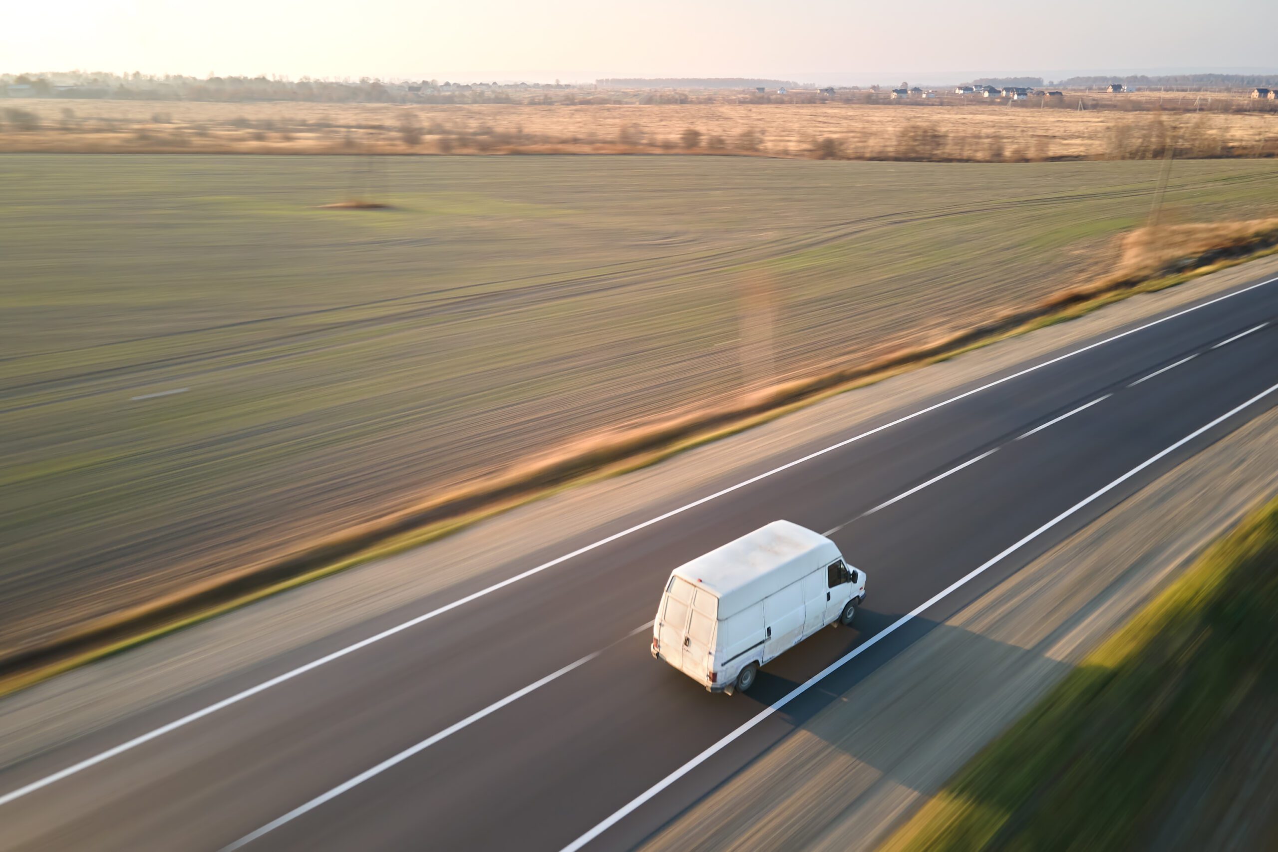 Aerial view of blurred fast moving cargo van driving on highway hauling goods. Delivery transportation and logistics concept