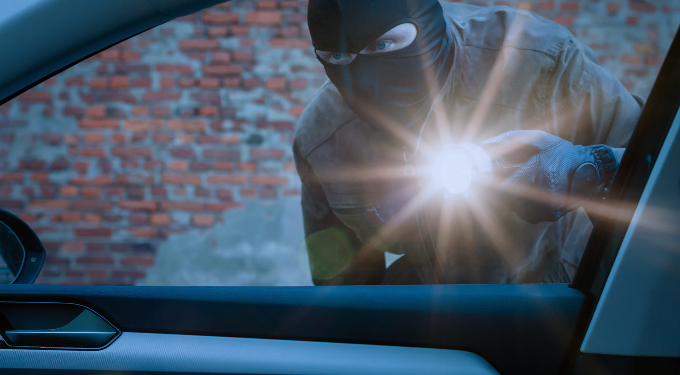 a car thief examines a car with a flashlight at night