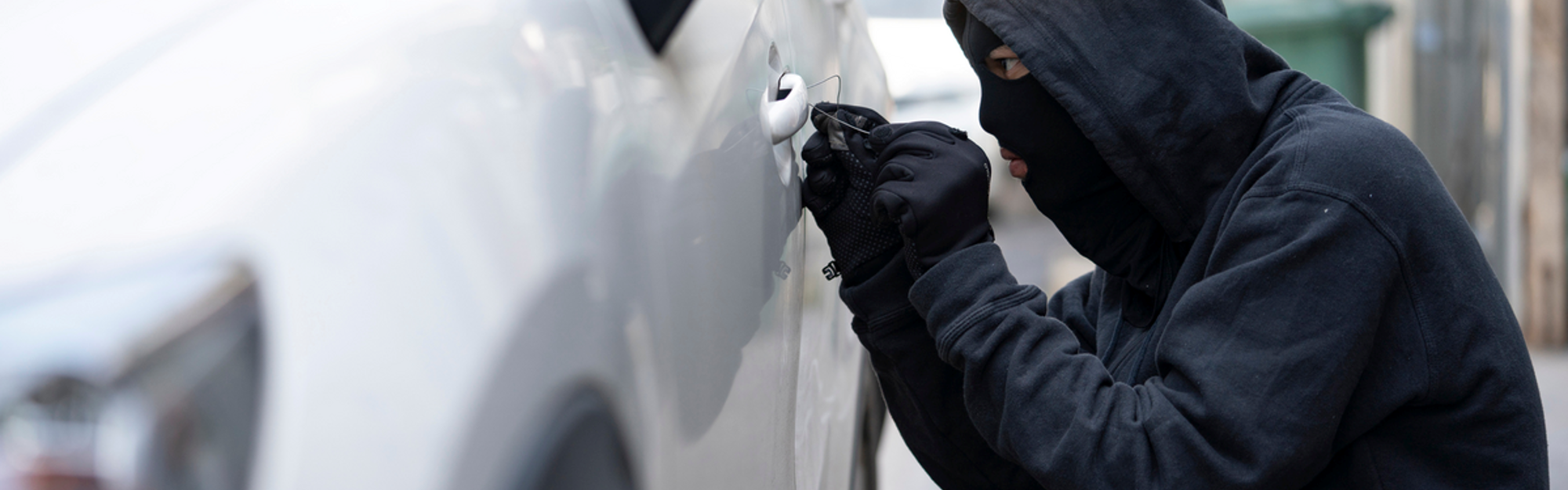 Thief dressed in black with a mask trying to steal a van.