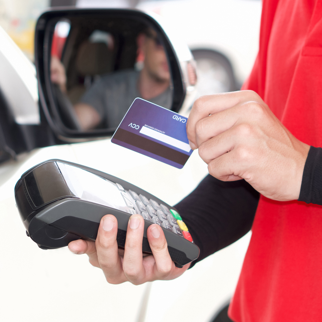 Gas station staff swipe credit card via payment terminal after giving a price quote to the customer sitting in the car.