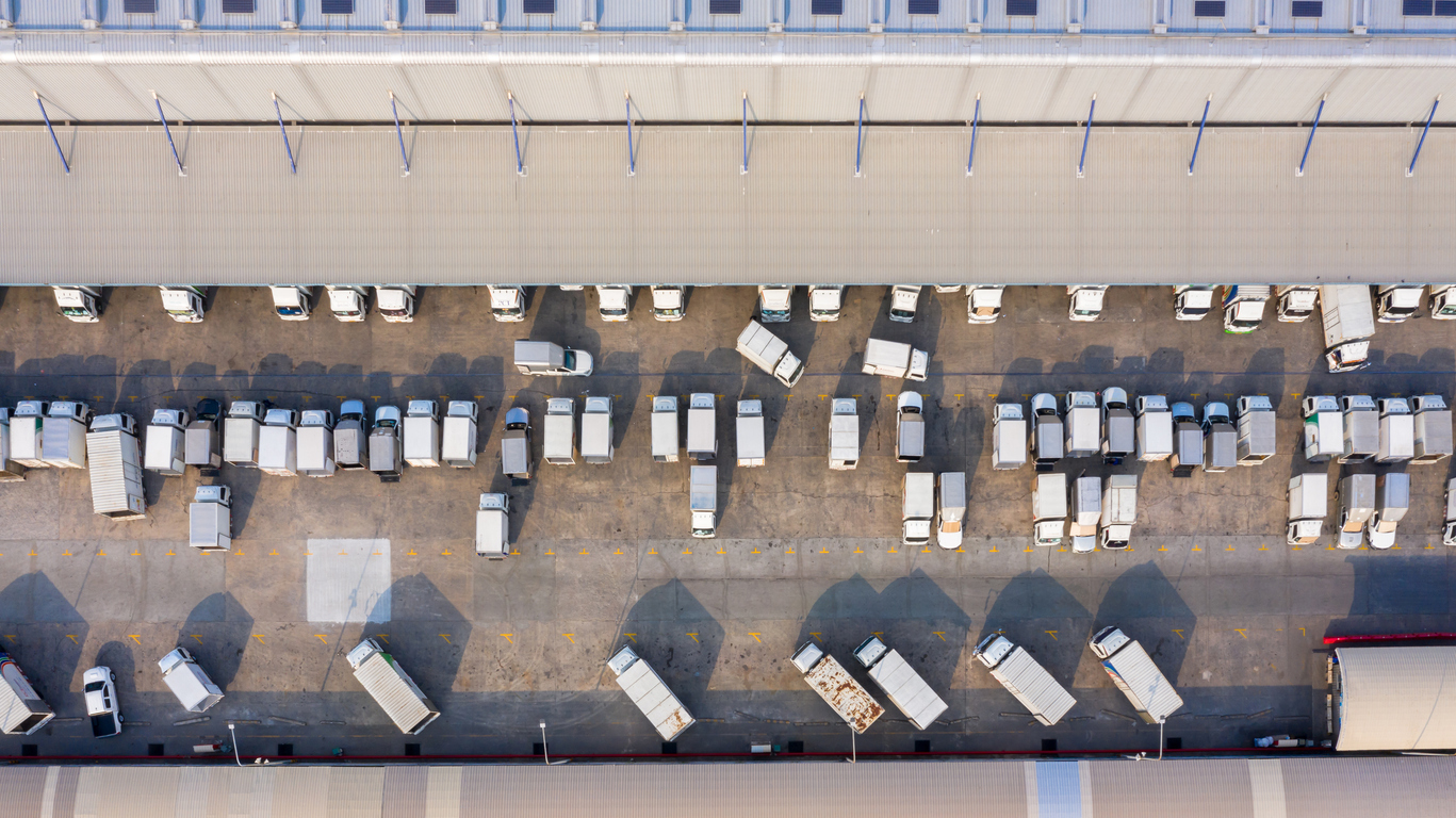 Aerial view logistics center in industrial city, Industrial warehouse loading dock where many truck with semi trailers load merchandise, Trucks loading at logistic center goods warehouse.