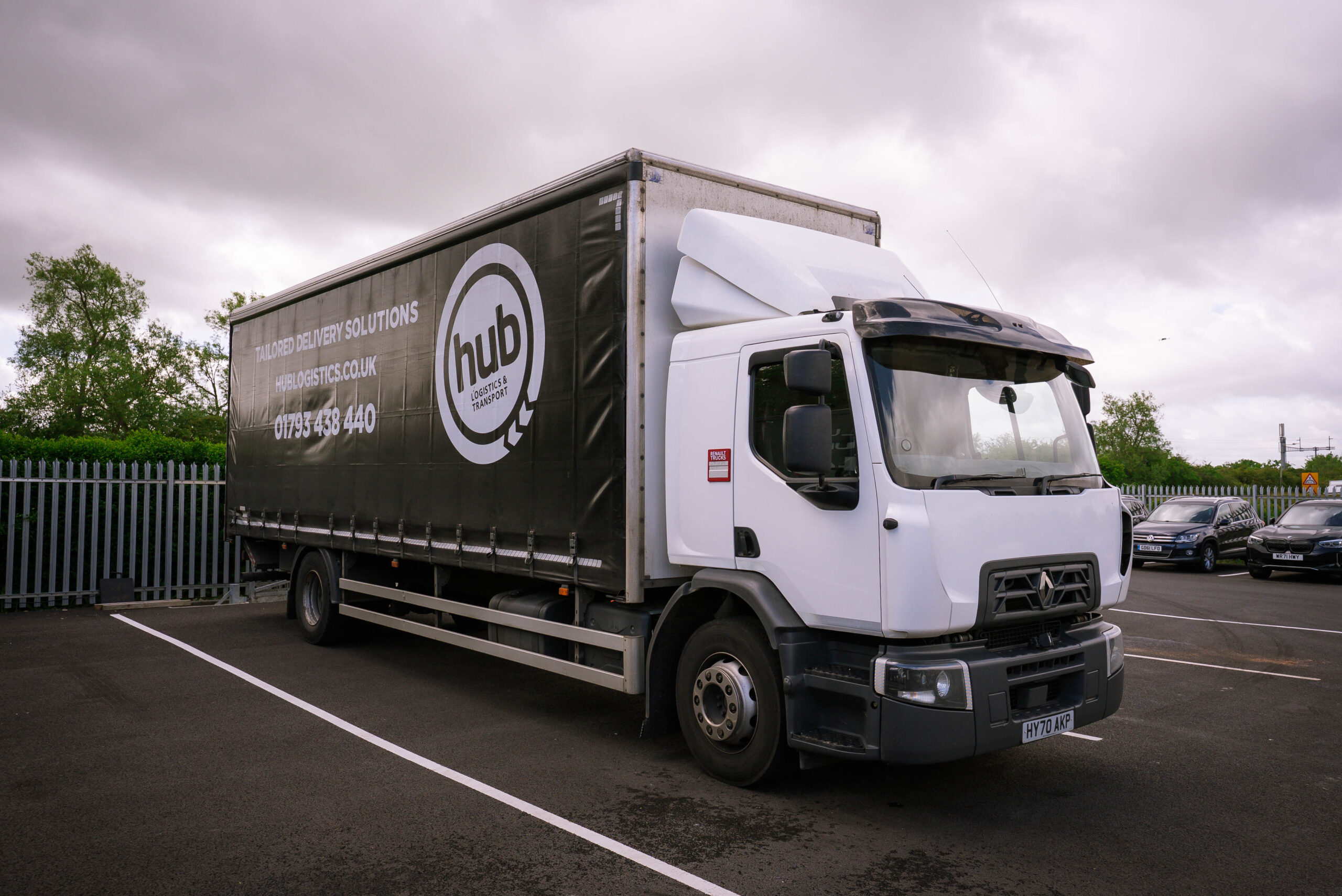 White delivery truck with a black trailer parked in a lot under cloudy skies; prominent hub logistics branding on the side panel store.
